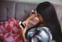 Жінка використовує мобільний телефон, розслабляючись на дивані у вітальні вдома — стокове фото