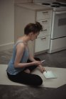 Здорова жінка використовує мобільний телефон і цифровий планшет на тренувальному килимку вдома — стокове фото
