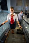 Personale femminile e passeggeri con bagagli in scala mobile in aeroporto — Foto stock