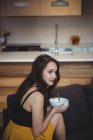 Woman sitting on sofa eating breakfast cereal in living room at home — Stock Photo
