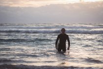 Ritratto di un uomo che porta la tavola da surf che esce dal mare al crepuscolo — Foto stock