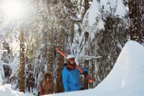 Pareja con esquí y snowboard caminando sobre una ladera nevada - foto de stock