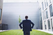 Rückansicht eines Geschäftsmannes, der mit den Händen auf der Hüfte vor einem Bürogebäude steht — Stockfoto