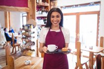 Портрет усміхненої офіціантки, що тримає чашку кави та закусок на супермаркеті — стокове фото