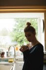 Mulher atenciosa segurando uma xícara de café na cozinha em casa — Fotografia de Stock