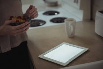 Media sezione di donna con ciotola di colazione in piedi vicino tablet digitale a casa — Foto stock