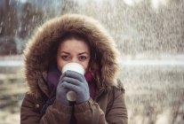 Portrait of beautiful woman in fur coat drinking coffee in winter — Stock Photo