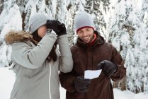 Casal com cartão de endereço olhando através de binóculos na paisagem nevada — Fotografia de Stock