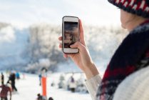 Primer plano de la mujer fotografiando esquiadores en la estación de esquí - foto de stock