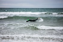 Man in wet suit swimming in sea on beach — Stock Photo