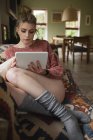 Donna seduta e con tablet digitale sul divano in soggiorno a casa — Foto stock