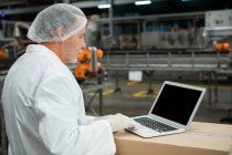 Вид сбоку рабочего-мужчины, использующего ноутбук на заводе по производству холодных напитков — стоковое фото