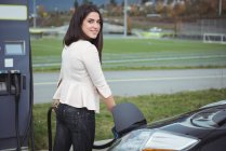 Schöne Frau lädt Elektroauto auf der Straße — Stockfoto