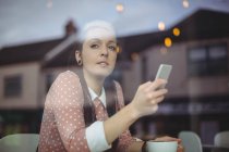 Продумана жінка використовує мобільний телефон, маючи каву в кафе — стокове фото