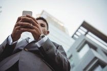 Низкий угол обзора бизнесмена с помощью мобильного телефона возле офисного здания — стоковое фото