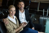 Retrato de pareja feliz usando teléfono móvil en el aeropuerto - foto de stock