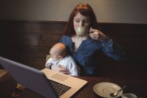 Mutter trinkt Kaffee, während sie Baby im Café hält — Stockfoto