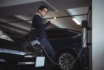 Man using mobile phone while charging electric car in garage — Stock Photo