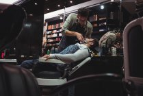 Homem ficando barba raspada por cabeleireiro com navalha na barbearia — Fotografia de Stock