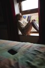 Женщина сидит на окне и читает книгу дома — стоковое фото