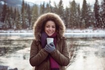 Vista frontal da mulher bonita em casaco de pele segurando xícara de café no inverno — Fotografia de Stock