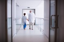 Vista trasera del médico caminando con el paciente en el pasillo del hospital - foto de stock
