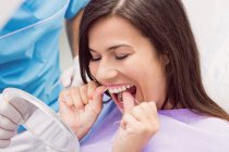 Paciente femenina que usa hilo dental en clínica dental - foto de stock
