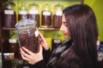 Mulher bonita segurando frasco de grãos de café no balcão na loja — Fotografia de Stock