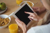 Casal usando tablet digital enquanto toma café da manhã em casa — Fotografia de Stock
