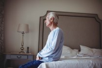 Homme âgé réfléchi assis sur le lit dans la chambre à coucher à la maison — Photo de stock
