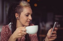 Donna che utilizza il telefono cellulare mentre prende il caffè nel caffè — Foto stock