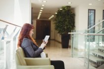 Donna d'affari incinta che utilizza tablet digitale vicino al corridoio in ufficio — Foto stock