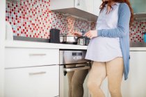 Mujer embarazada cocinando alimentos en la cocina en casa - foto de stock