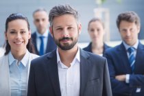Portrait d'un homme d'affaires confiant avec des collègues debout devant un immeuble de bureaux — Photo de stock