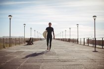 Surfeur marche avec planche de surf sur la jetée à la plage — Photo de stock