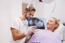 Стоматолог, який показує рентгенівський знімок пацієнтки у клініці — стокове фото