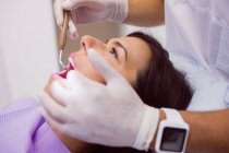 Крупный план стоматолога, осматривающего женские зубы с зеркалом во рту — стоковое фото