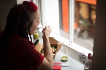Mulher olhando pela janela enquanto come uma salada no café — Fotografia de Stock