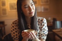 Femme réfléchie prenant une tasse de café au café — Photo de stock