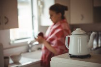 Kettle on stove and woman standing in background in kitchen at home — Stock Photo