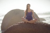 Hermosa mujer realizando yoga sobre roca en día soleado - foto de stock
