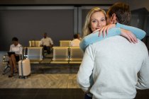 Счастливая пара обнимает друг друга в зоне ожидания в аэропорту — стоковое фото