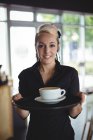 Porträt einer Kellnerin, die mit einer Tasse Kaffee im Café steht — Stockfoto