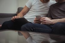 Couple gay assis sur le canapé et regardant tablette numérique à la maison — Photo de stock