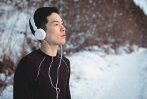 Задумчивый человек, слушающий музыку в наушниках зимой — стоковое фото