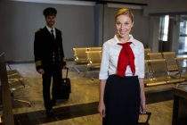 Porträt eines Piloten und einer Stewardess, die mit ihren Trolleytaschen im Flughafenterminal spazieren gehen — Stockfoto