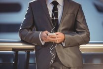 Mid section of businessman listening to music and using mobile phone near office building — Stock Photo