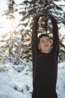 Homem sorridente esticando os braços na floresta durante o inverno — Fotografia de Stock