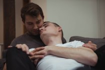 Romântico gay casal abraçando no sofá na sala de estar em casa — Fotografia de Stock