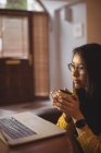 Женщина пьет кофе дома, пользуясь ноутбуком — стоковое фото